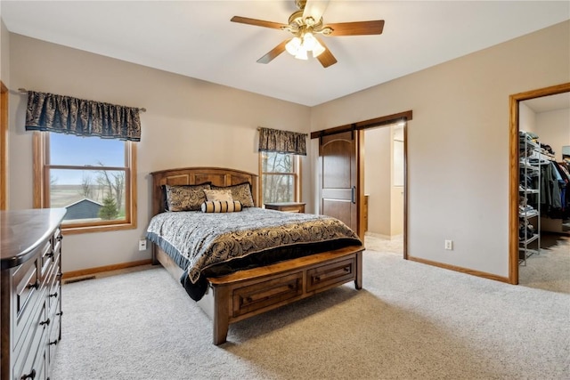 bedroom featuring light colored carpet, baseboards, a walk in closet, ceiling fan, and a barn door
