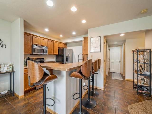 kitchen featuring brown cabinets, a breakfast bar area, stainless steel appliances, and recessed lighting