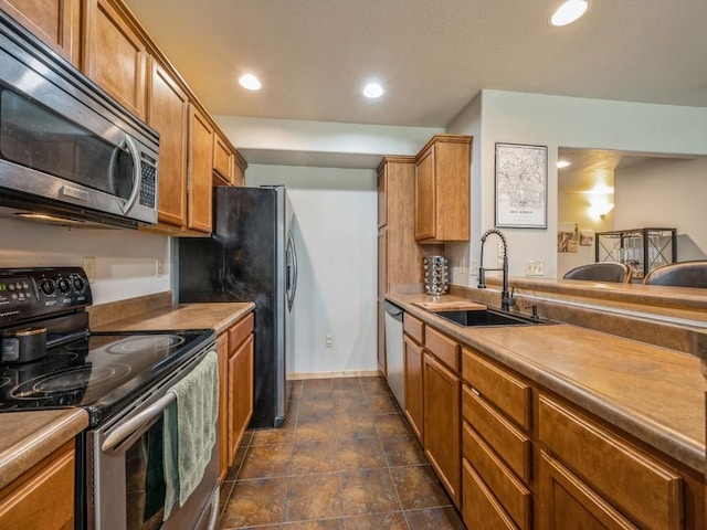 kitchen with brown cabinets, recessed lighting, stainless steel appliances, a sink, and baseboards