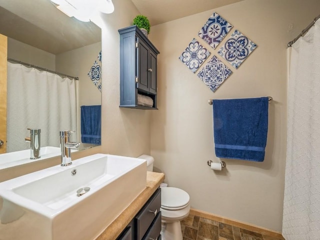 full bathroom with stone finish flooring, vanity, toilet, and baseboards