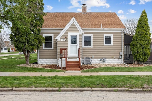 bungalow-style home with a shingled roof, a chimney, a front yard, and cooling unit