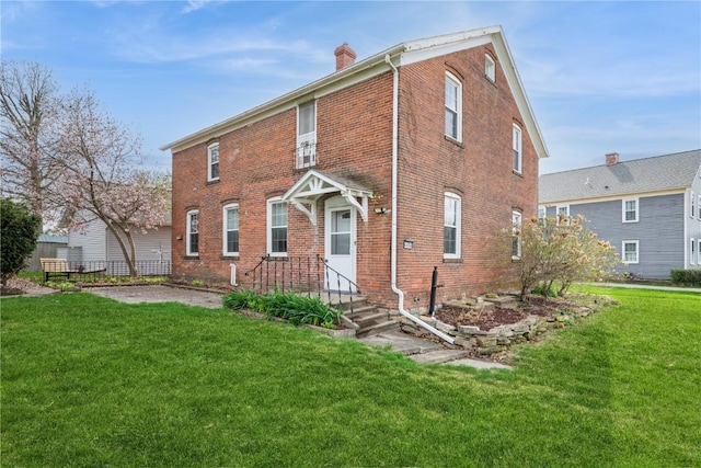 back of house with a lawn, a chimney, and brick siding