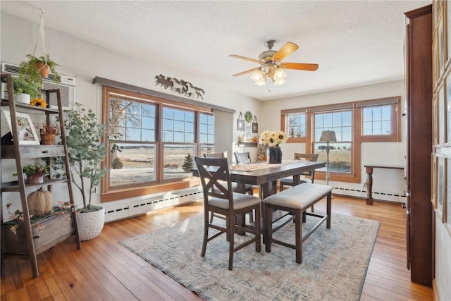 dining space with a baseboard heating unit, a textured ceiling, light wood-style flooring, and a ceiling fan