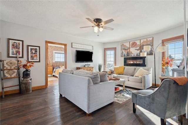 living area featuring a ceiling fan, a wealth of natural light, baseboards, and dark wood-style floors