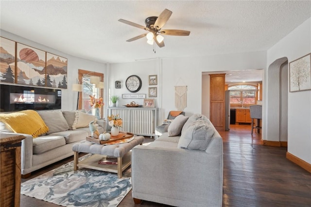 living room with a textured ceiling, baseboards, a ceiling fan, and wood finished floors