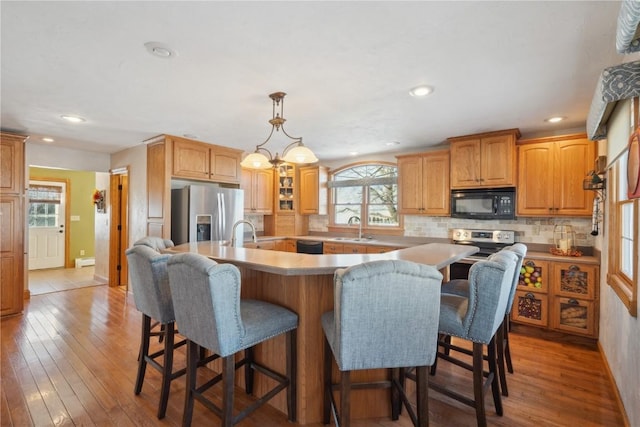 kitchen featuring black appliances, light wood finished floors, an island with sink, and a sink