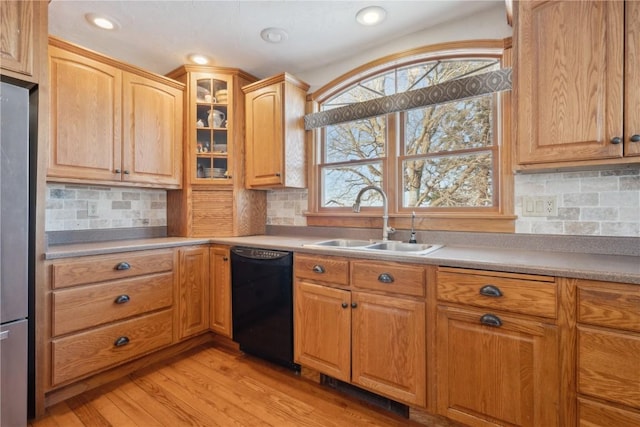 kitchen featuring light wood finished floors, glass insert cabinets, a sink, freestanding refrigerator, and black dishwasher