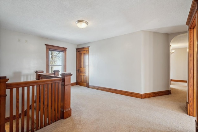 interior space featuring carpet, an upstairs landing, a textured ceiling, baseboards, and arched walkways