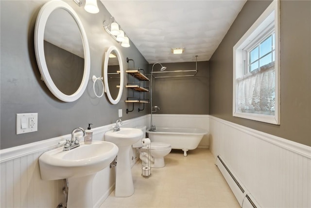 full bath with toilet, a sink, a freestanding bath, wainscoting, and baseboard heating