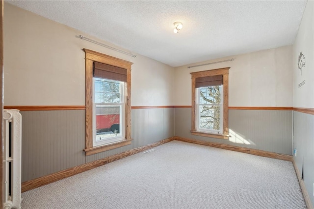 spare room featuring radiator, a wainscoted wall, a textured ceiling, and carpet floors