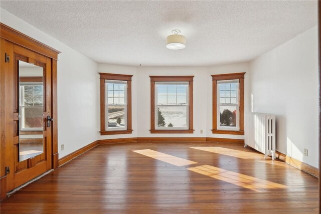 spare room featuring baseboards, a wealth of natural light, radiator heating unit, and wood-type flooring