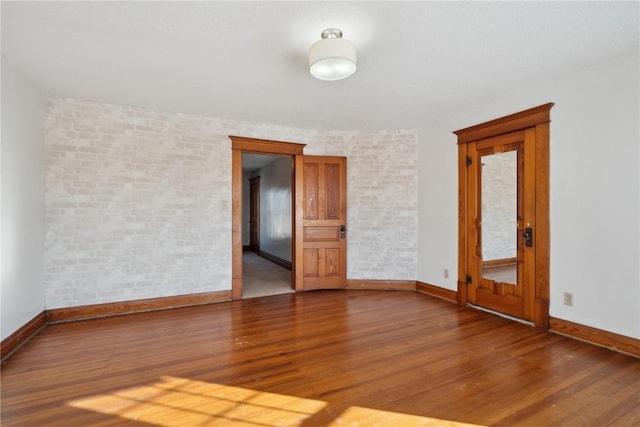 empty room with baseboards, brick wall, and wood finished floors