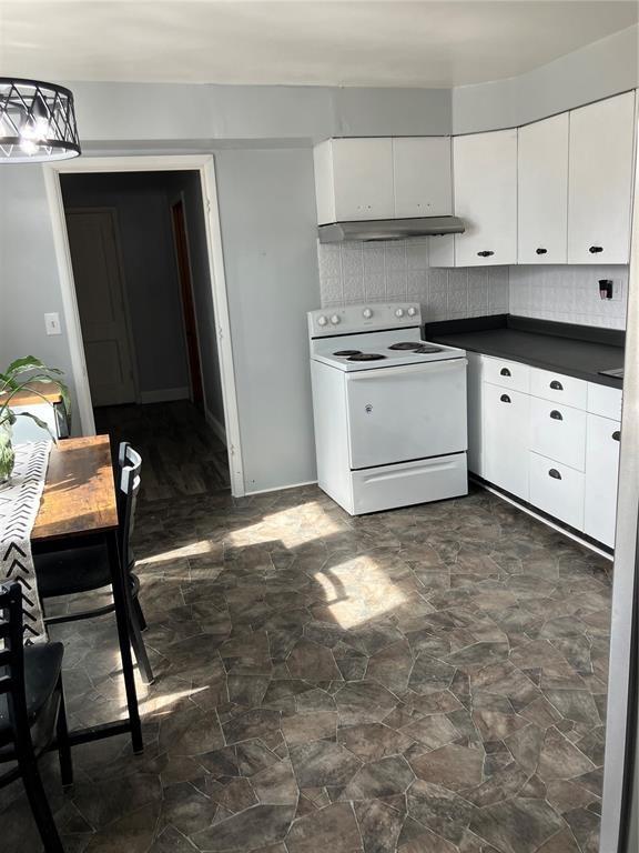 kitchen with under cabinet range hood, stone finish flooring, dark countertops, white range with electric stovetop, and white cabinetry