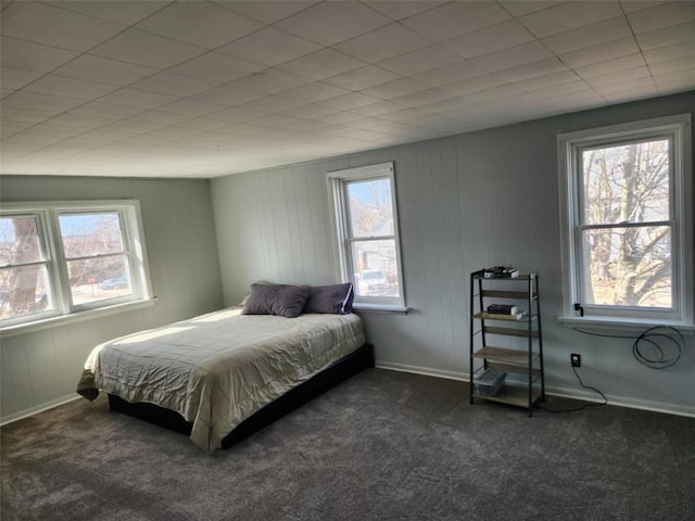 bedroom with baseboards, wood walls, and carpet