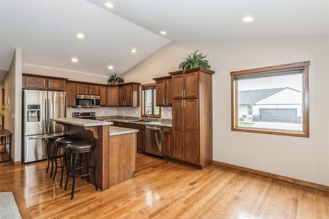 kitchen with a sink, a center island, a breakfast bar area, appliances with stainless steel finishes, and lofted ceiling