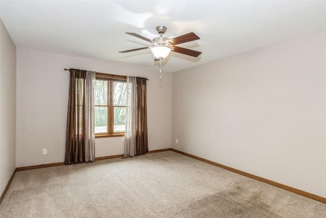 spare room featuring a ceiling fan, light colored carpet, and baseboards