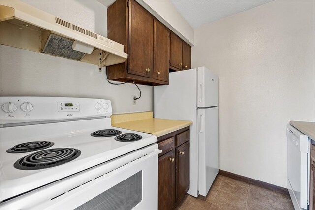 3212 Wilson Ave SW, Cedar Rapids, IA 52404 - kitchen featuring white appliances, under cabinet range hood, dark brown cabinets, and baseboards