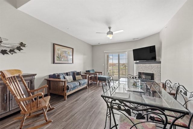 living area featuring a ceiling fan, a stone fireplace, and wood finished floors