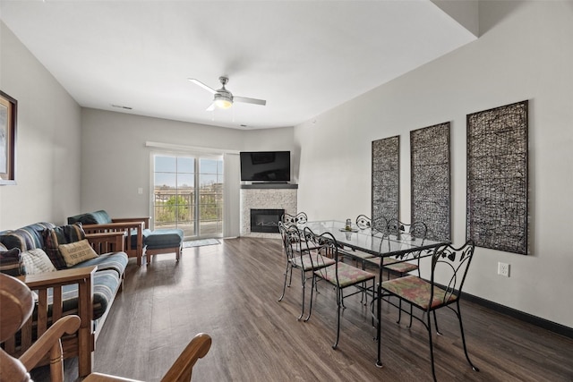 dining room with a glass covered fireplace, ceiling fan, baseboards, and dark wood finished floors