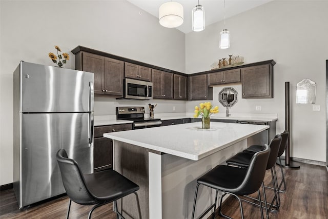 kitchen featuring dark brown cabinetry, a breakfast bar, appliances with stainless steel finishes, and dark wood finished floors