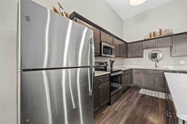 kitchen with a sink, appliances with stainless steel finishes, light stone counters, dark brown cabinets, and dark wood finished floors