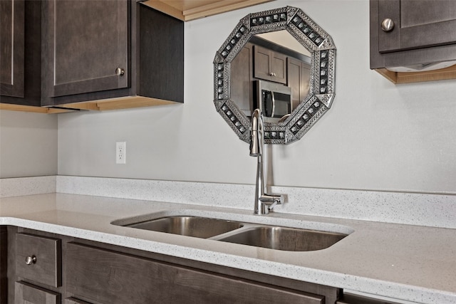 kitchen with stainless steel microwave, dark brown cabinetry, a sink, and light stone counters