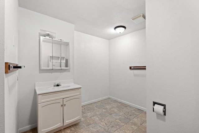 bathroom featuring stone finish floor, visible vents, vanity, and baseboards