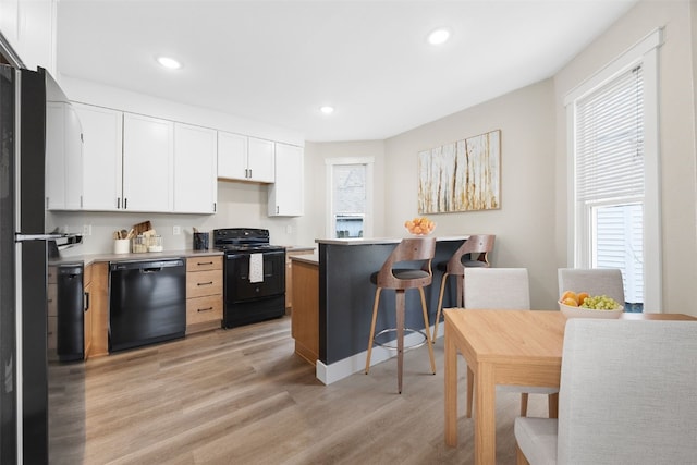317 16th St NE, Cedar Rapids, IA 52402 - kitchen featuring black appliances, a breakfast bar area, plenty of natural light, light wood-style flooring, and recessed lighting