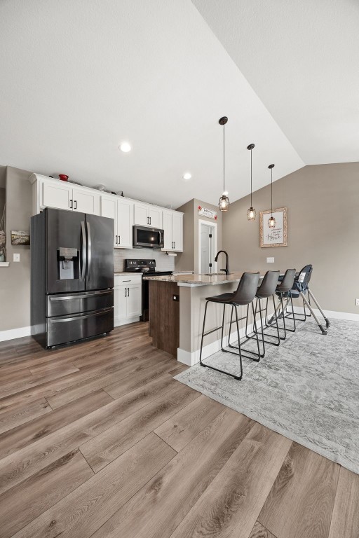 5116 Ruhd St SW, Cedar Rapids, IA 52404 - kitchen featuring stainless steel appliances, a kitchen bar, vaulted ceiling, white cabinets, and light wood-style flooring