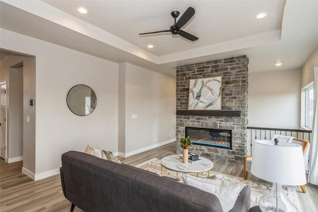 living area featuring a fireplace, a raised ceiling, a ceiling fan, baseboards, and wood finished floors