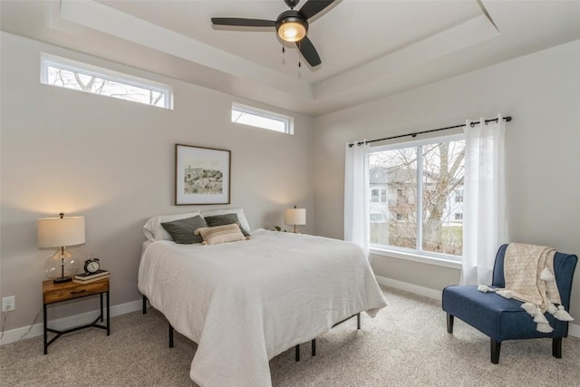 carpeted bedroom with ceiling fan, a raised ceiling, and baseboards