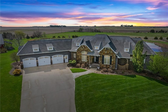 view of front of home featuring a front lawn, a rural view, driveway, stone siding, and an attached garage