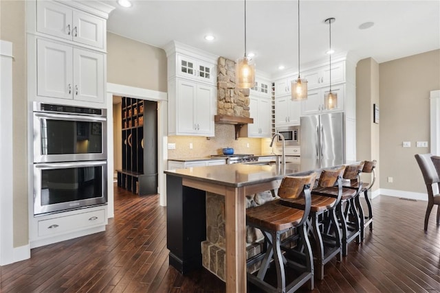 kitchen with a sink, baseboards, appliances with stainless steel finishes, and dark wood-type flooring