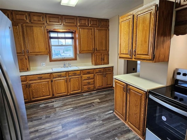 kitchen featuring appliances with stainless steel finishes, a sink, brown cabinetry, and dark wood finished floors