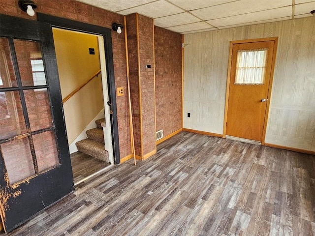 unfurnished room featuring wooden walls, stairs, visible vents, and wood finished floors