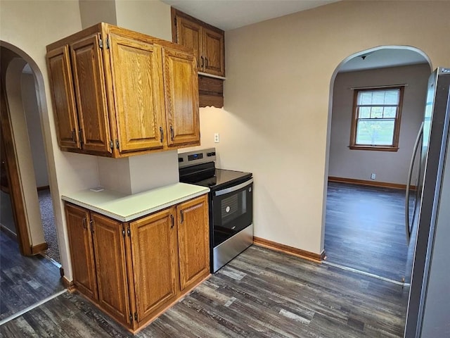kitchen featuring dark wood-style flooring, baseboards, light countertops, arched walkways, and appliances with stainless steel finishes