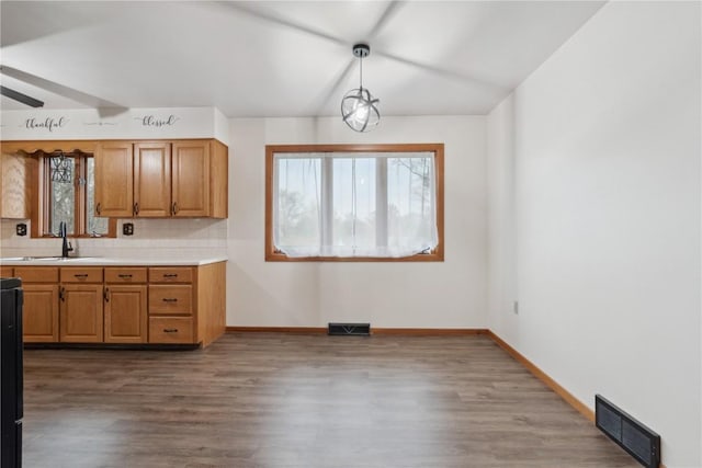 kitchen featuring visible vents, wood finished floors, baseboards, light countertops, and a sink