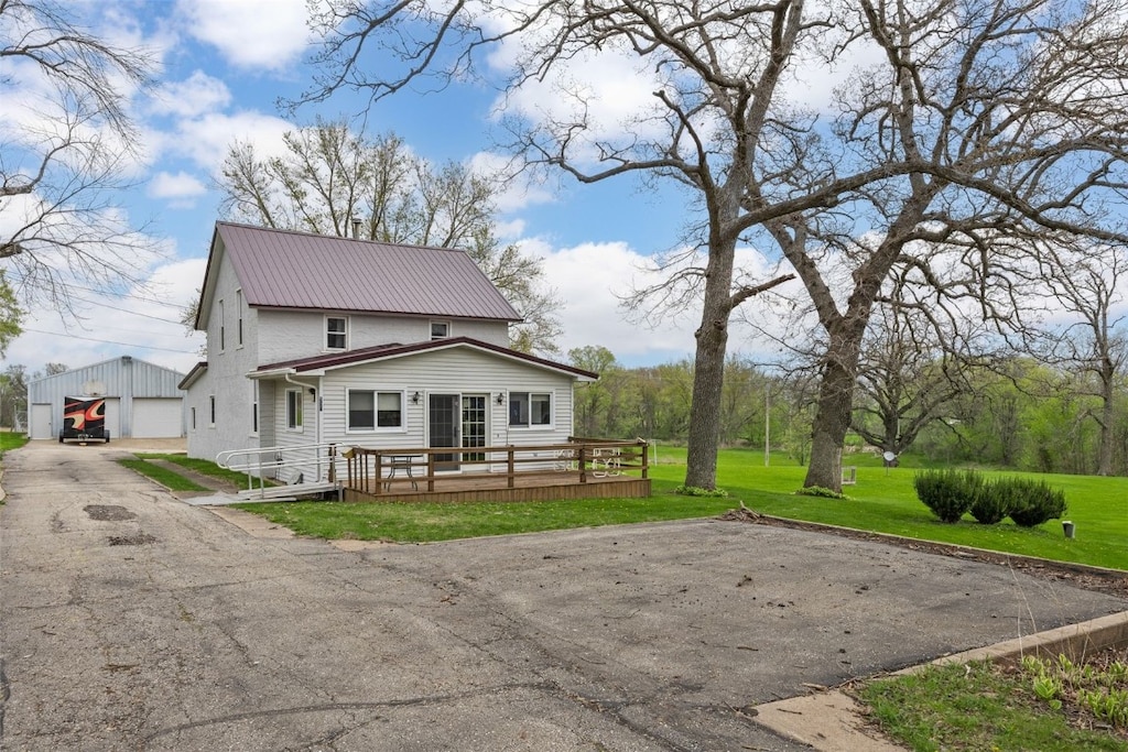 rear view of property with metal roof, a lawn, a deck, a garage, and an outdoor structure