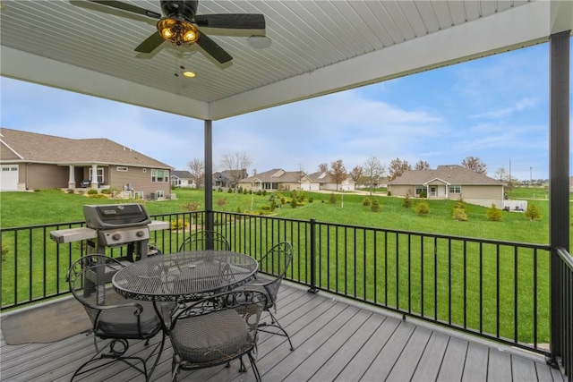 wooden terrace featuring a lawn, a ceiling fan, outdoor dining area, and a residential view