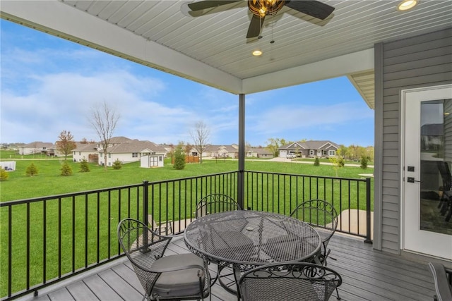 wooden terrace featuring outdoor dining area, ceiling fan, a lawn, and a residential view