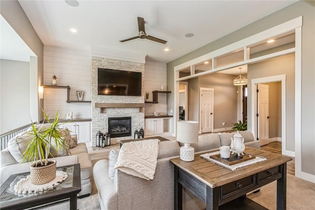 living area with recessed lighting, ceiling fan, a stone fireplace, and baseboards