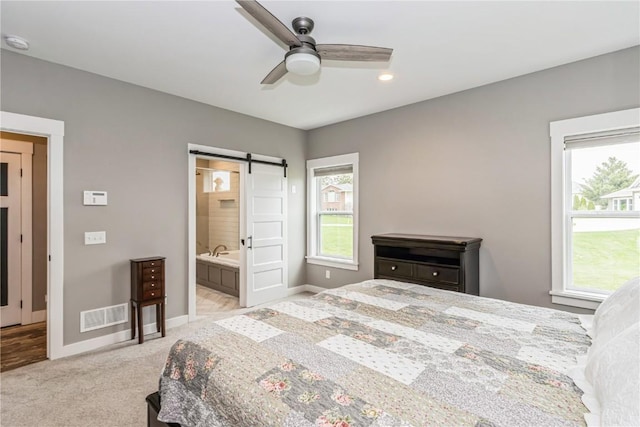 carpeted bedroom featuring connected bathroom, ceiling fan, a barn door, baseboards, and visible vents
