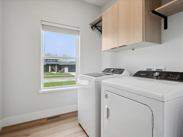 washroom with washer and clothes dryer, cabinet space, baseboards, light wood-style flooring, and a wealth of natural light