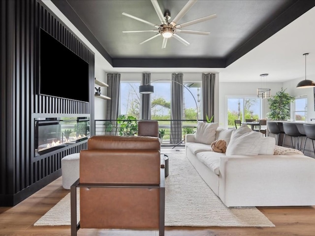 living area with a healthy amount of sunlight, a ceiling fan, a glass covered fireplace, and wood finished floors