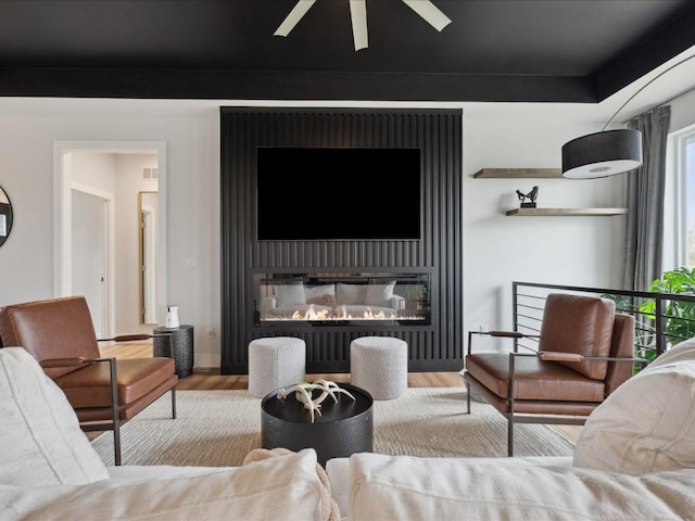 living room featuring a ceiling fan, a glass covered fireplace, and wood finished floors