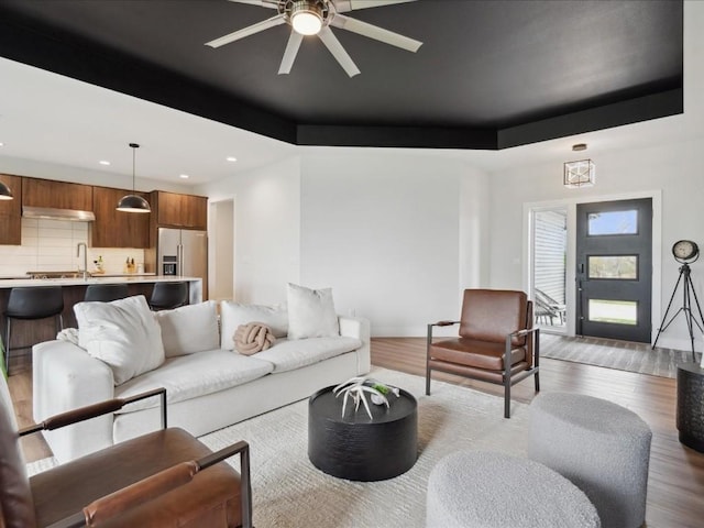 living room featuring a ceiling fan, recessed lighting, a raised ceiling, and light wood-type flooring