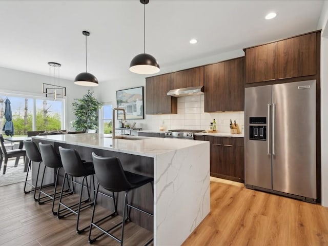 kitchen with decorative backsplash, a kitchen breakfast bar, high end refrigerator, a sink, and an island with sink