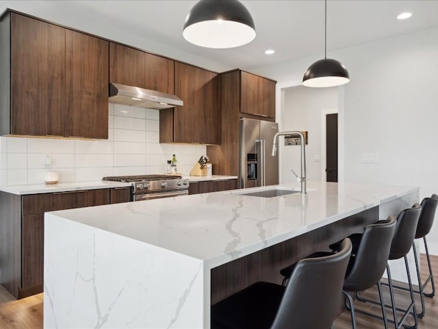 kitchen featuring decorative backsplash, modern cabinets, under cabinet range hood, a sink, and stainless steel appliances