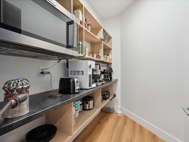 interior space with dark countertops, open shelves, light wood-style flooring, baseboards, and stainless steel microwave