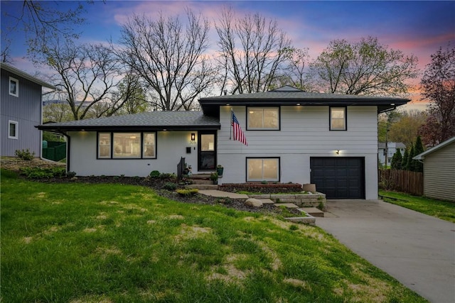 tri-level home with a garage, a yard, driveway, and fence